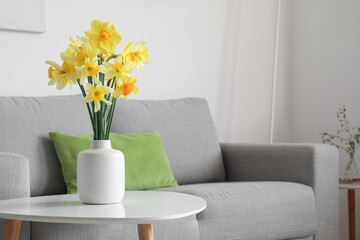 Vase with blossoming narcissus flowers on coffee table in living room