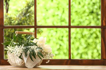 Basket with beautiful tulip and gypsophila flowers on windowsill