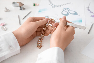 Female jeweler making adornment on white table, closeup