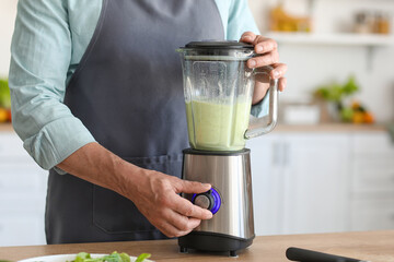 Mature man making smoothie with blender in kitchen, closeup