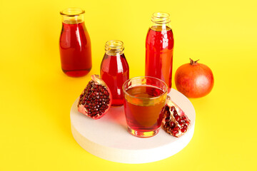 Fototapeta na wymiar Bottles and glass of fresh pomegranate juice on yellow background