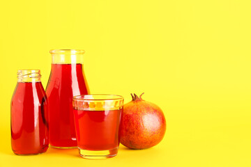 Bottles and glass of fresh pomegranate juice on yellow background