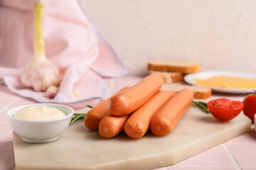 Board of tasty sausages with rosemary and mayonnaise on pink tile background