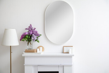 Vase with lilac flowers, books and candles on fireplace in light room