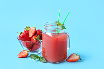 Mason jar of juice and bowl with strawberry on blue background