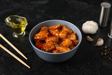 Tasty sweet and sour chicken in bowl with spices on dark background