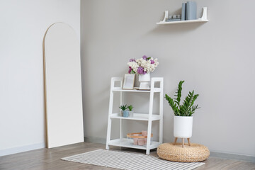 Interior of light room with lilac flowers in vase and shelving unit