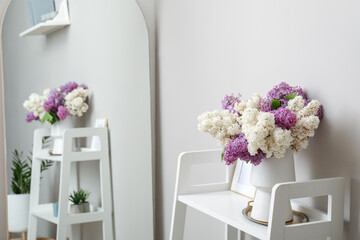 Vase with lilac flowers and frame on shelf in light room