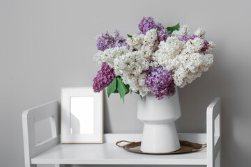 Vase with lilac flowers and frame on shelf in light room
