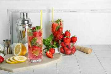 Glass of fresh strawberry mojito with shaker and jigger on white tile table