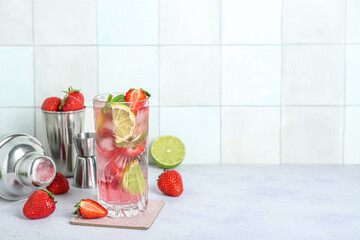 Glass of fresh strawberry mojito with jigger and shakers on grunge light table