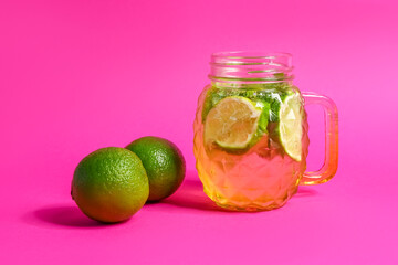 Mason jar of cold mojito and lime on pink background