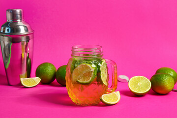 Mason jar of cold mojito and shaker with lime on pink background