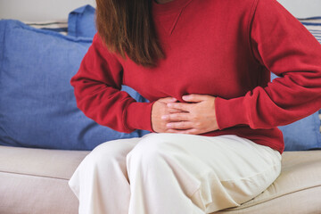 Closeup image of a sick woman suffering from stomachache, abdominal pain while sitting on sofa at home