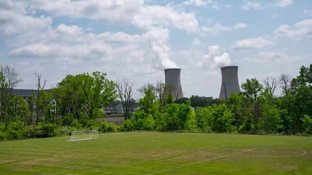 Time lapse of nuclear reactor Power Plant with a soccer field in front on a warm cloudy day in the suburbs 