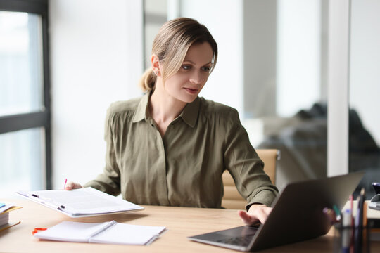 Focused woman types on keyboard of laptop holding clipboard