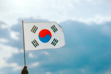 Hand Waving the Flag of South Korea on a Beautiful Sky. Optimistic person holding national flag...