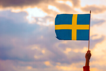 Hand Waving the Flag of Sweden on a Beautiful Sky. Optimistic person holding Swedish flag...
