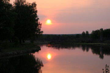 Fototapeta na wymiar A colorful sunset over a calm river among birch groves. Summer evening.