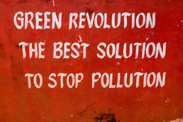 A white inscription painted on a red wall. The Green Revolution stands as the optimal solution to halt pollution, paving the way for a sustainable and eco-friendly future.
