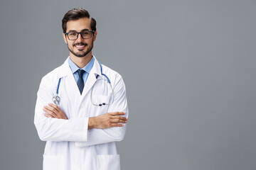 A serious doctor man in a white coat and eyeglasses and a stethoscope looks at the camera on a gray...