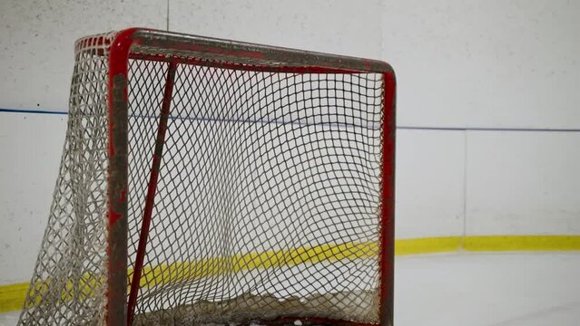 A hockey puck being fired into a net during practice at a hockey rink.