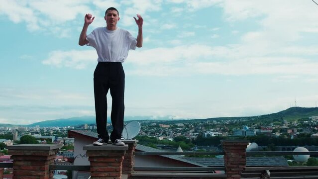 A guy in a white T-shirt is dancing a modern dance on the streets of the old city. Historical streets of Tbilisi. A young dancer improvises in a dance against a clear, blue sky.