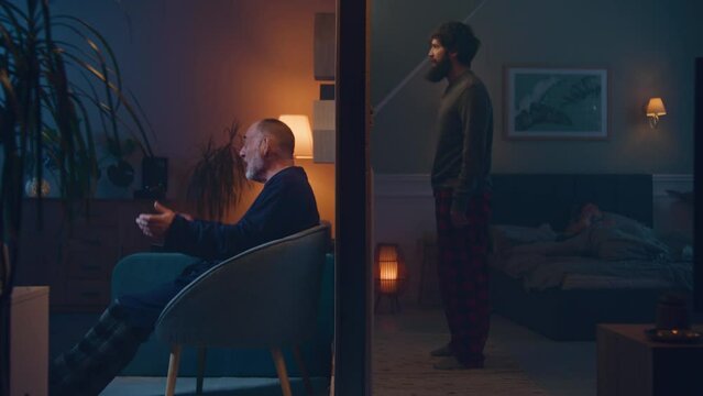 Elderly man watch funny TV show, laughs and interferes with sleep neighbours late at night. Man screams, knocks on the wall and goes to bed. Low level of noise insulation. Concept of neighbourhood.