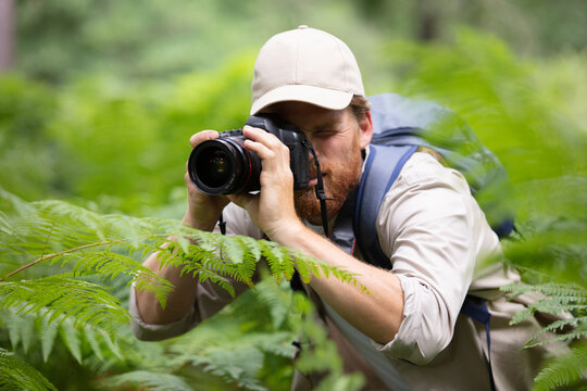 man trekking among trees and taking pictures with dslr camera