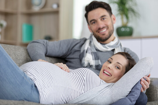 photo of happy pregnant woman and man on gray sofa