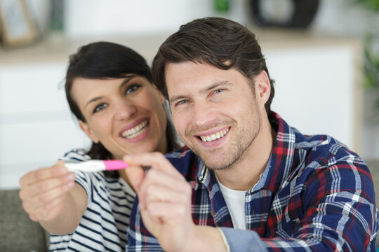 happy couple hugging while holding positive pregnancy test
