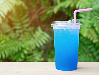 Cold blue drink with squash in plastic glass placed on wooden floor, blurred green leaf background. Leave the copy area active.