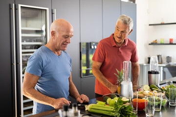 Happy senior caucasian male friends talking and preparing healthy smoothies together in kitchen