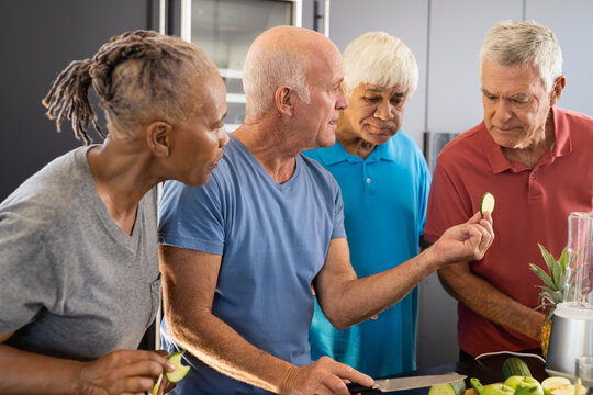 Happy diverse senior friends discussing ingredients for preparing healthy smoothies in kitchen
