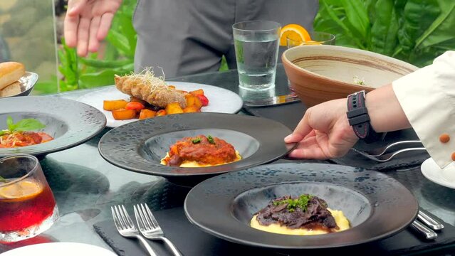 Guests at a luxury resort restaurant are served by a waiters at a table with a tropical view. The elegant setting adds to the romance of the dining experience.