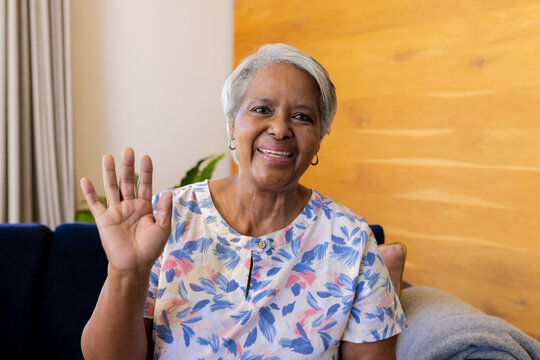 Happy senior biracial woman making video call smiling and waving sitting on sofa at home