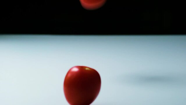 Slow Motion Shot of Tomatoes of Different Colors Falling, Bouncing and Rolling onto a White Surface untill they Stop Moving