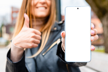 Young smiling woman showing mockup and thumb up on the city street.Mockup,advertisement.Selective focus,blurred background.