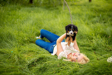 A beautiful girl with a dog sits in the park on the grass. Love to the animals. Home pet on a walk. Animal protection. Bernese mountain dog puppy.