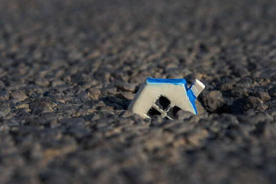 Miniature White Toy House Fallen Into A Crack In The Earth.Closeup.Copy Space.