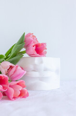 Pink tulips bouquet and plaster statue of lips lying on white wrinkled blanket background copy space