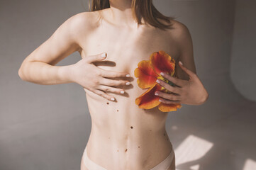 Girl in underwear with red tulip close breasts. Breast cancer awareness concept. Naked young woman covers breasts with hands. 
Topless female with breast covered with flowers cropped image  - obrazy, fototapety, plakaty