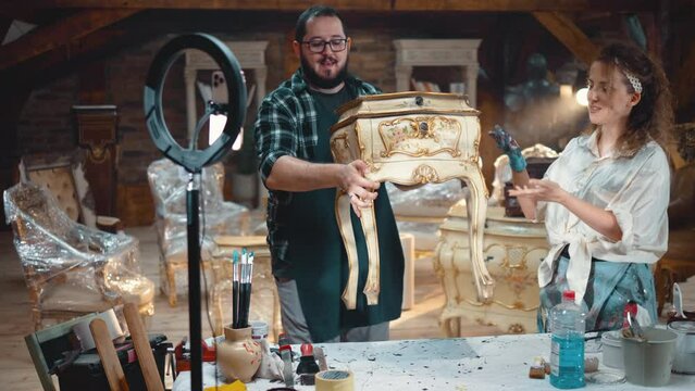 Owners of the antique store broadcast live streaming at the retro furniture shop, they are talking and presenting a chest of drawers in front of the phone camera. Online auction sale