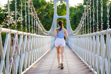 A focused young woman jogs across a bridge in a park, showcasing an active and healthy lifestyle.
