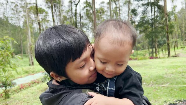 Asian boy kissing his brother at the forest park. Family bonding and recreation on weekend.