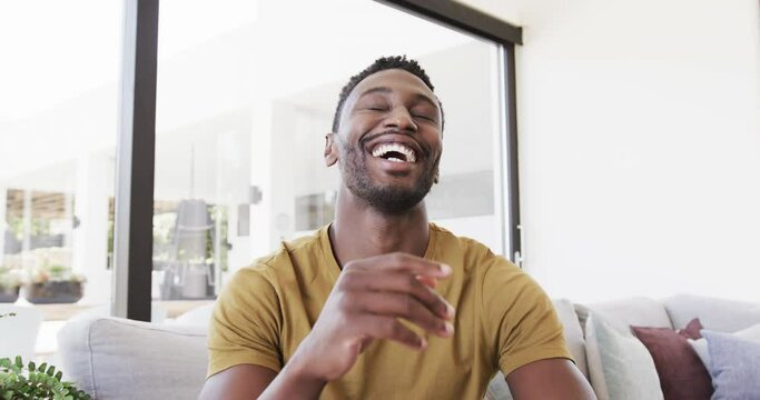 Portrait of happy african american man making video call, talking and laughing, in slow motion