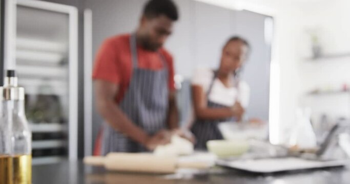 Happy african american couple in aprons baking together, kneading dough in kitchen, slow motion