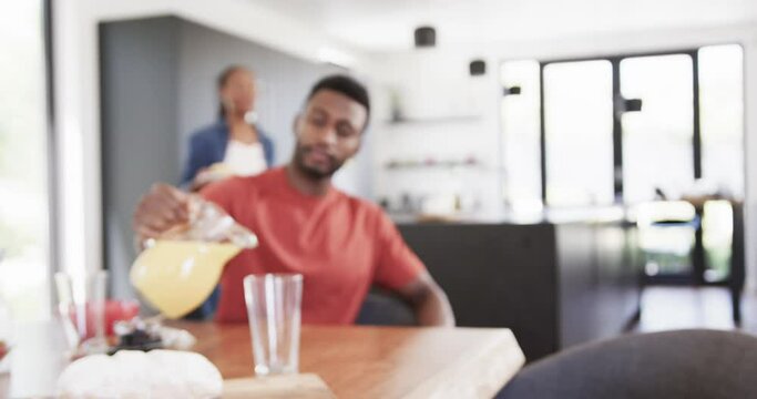 Happy african american couple pouring juice and serving breakfast in sunny kitchen, slow motion
