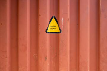 Rusty red shipping container with yellow and black triangle warning label reading 
