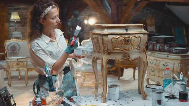 Female restorer apply putty to an old antique chest of drawers in a creative art wood shop. Workshop for the restoration and sale of old antique furniture